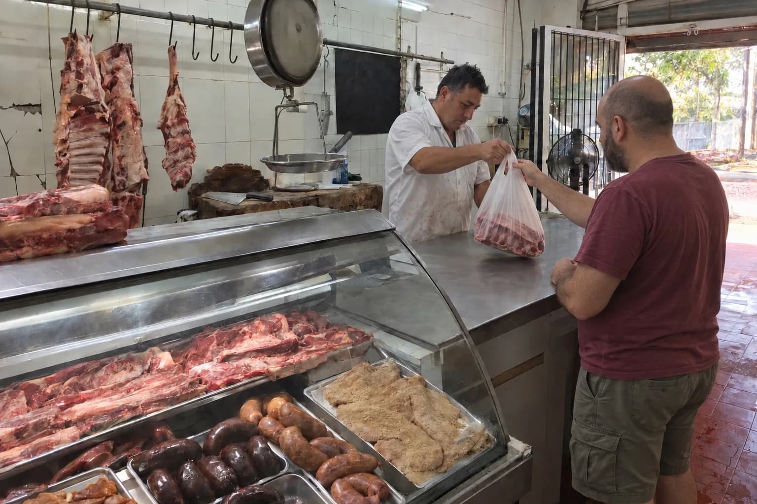 Carnicero entregando una compra por encima de la vitrina de cortes, chorizos y milanesas
